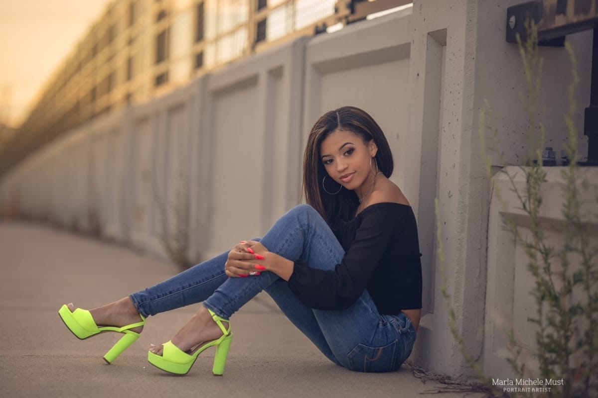 Detroit-area High school senior picture photographer captures a graduation photo of a girl in stylish high heels leaning against a structural support of a downtown Detroit building