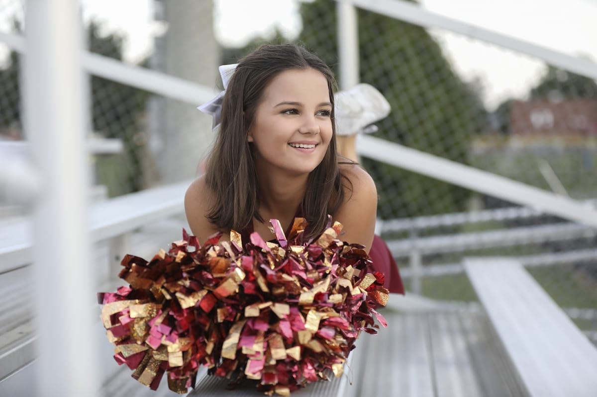 Detroit-area High school senior photographer captures a graduation photo of a girl laying on the bleachers of a Michigan high school stadium with pom poms in the foreground.