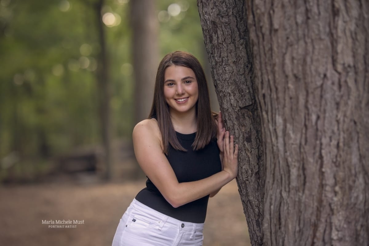 Detroit-area High school senior photographer captures a graduation photo of a girl leaning against a tree and smiling.
