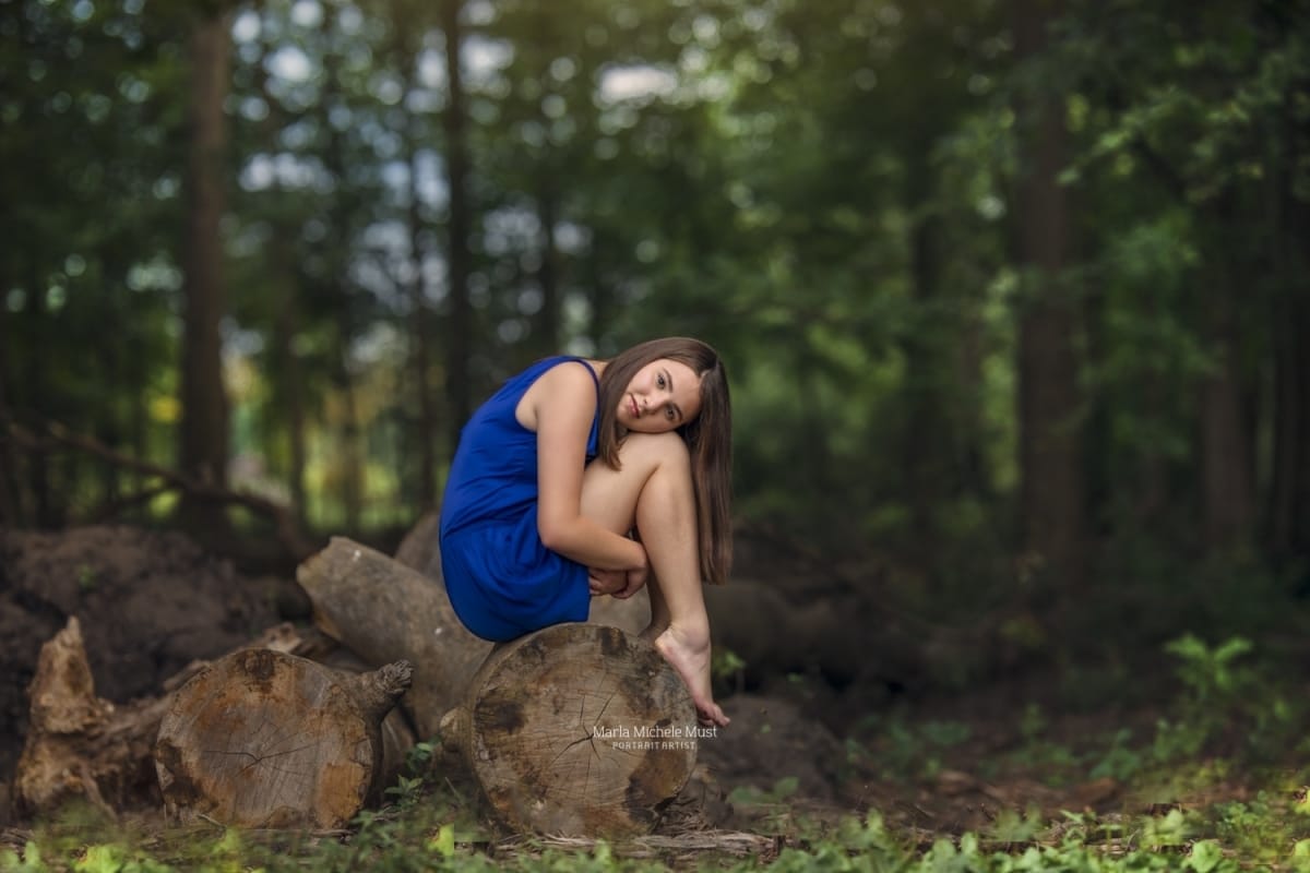 Detroit-area High school senior photographer captures the portrait of a girl sitting on a rock and holding her knees in a Michigan park