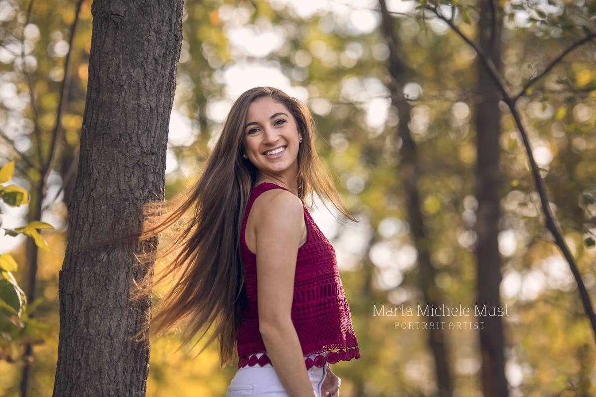 High school senior poses for her senior pictures as she smiles over her shoulder in a Michigan park