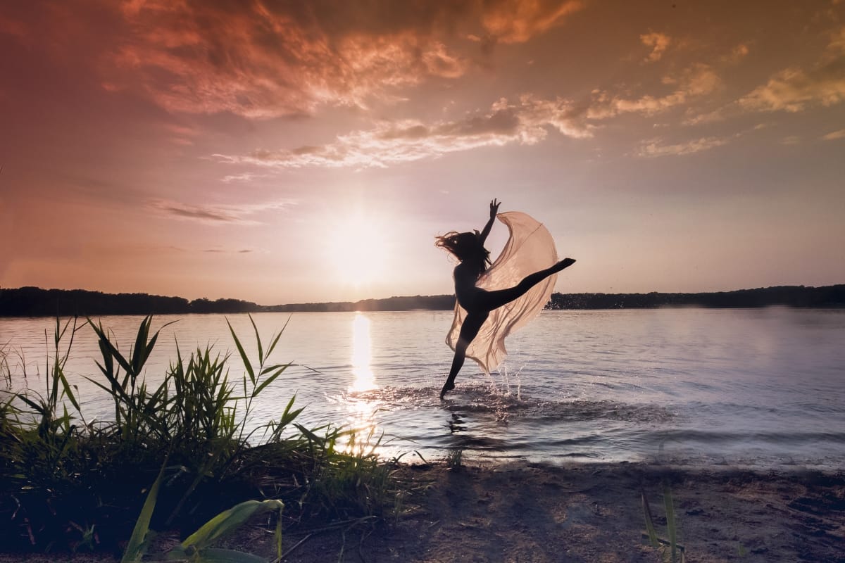 Skilled dancer exhibits ethereal grace with a soaring leap, beautifully photographed by a Detroit-based portrait photographer at sunset in a lake.