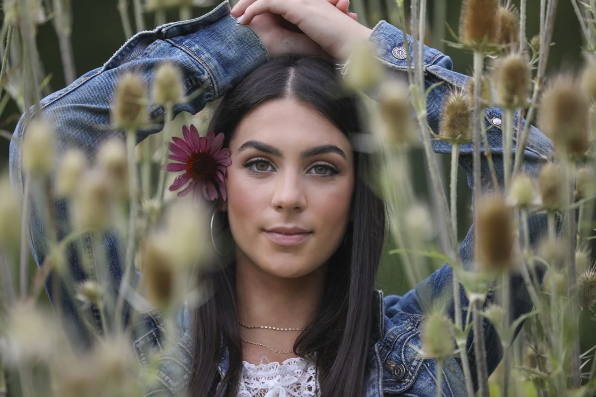 Wildflowers surround the frame of a high school senior girl as she poses for her graduation photoshoot
