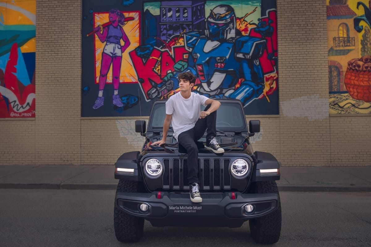 High school senior poses on the hood of a Jeep for his senior portrait in Detroit