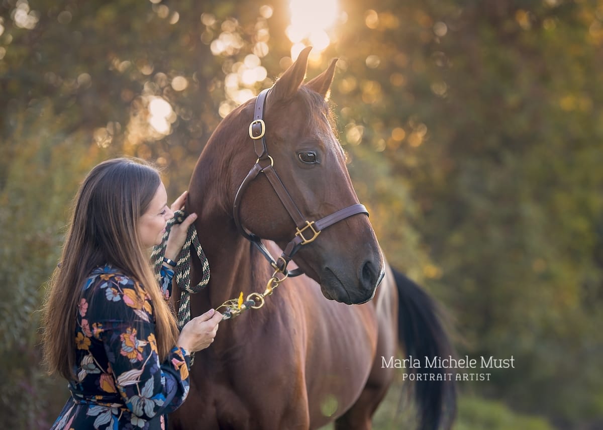 Horse owner portrait for a Detroit equine photographer: Embracing the horse's nose with care, a golden sunset peeking out behind them.