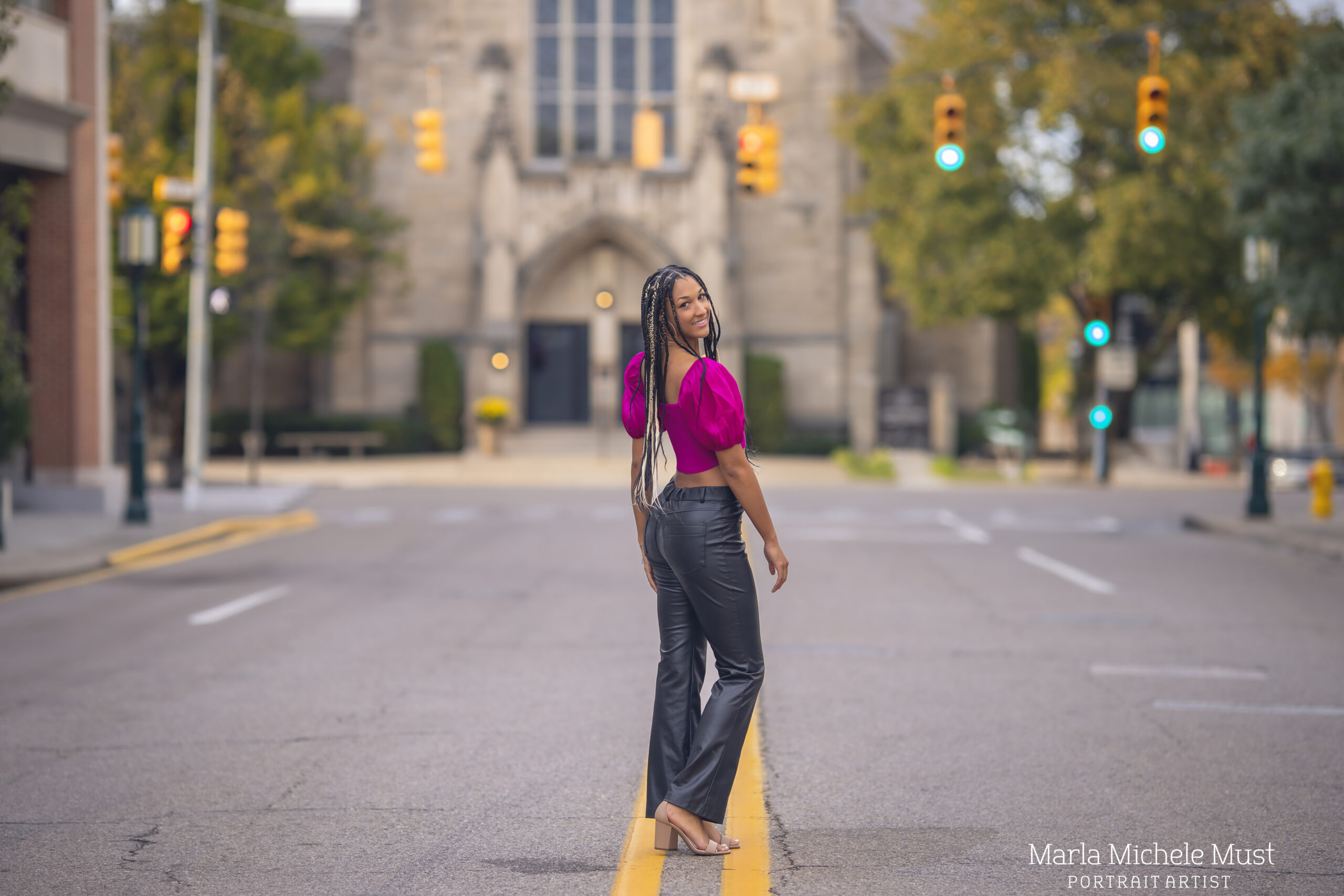 A young woman poses for her senior portrait photoshoot in the street of a downtown Metro in front of a church
