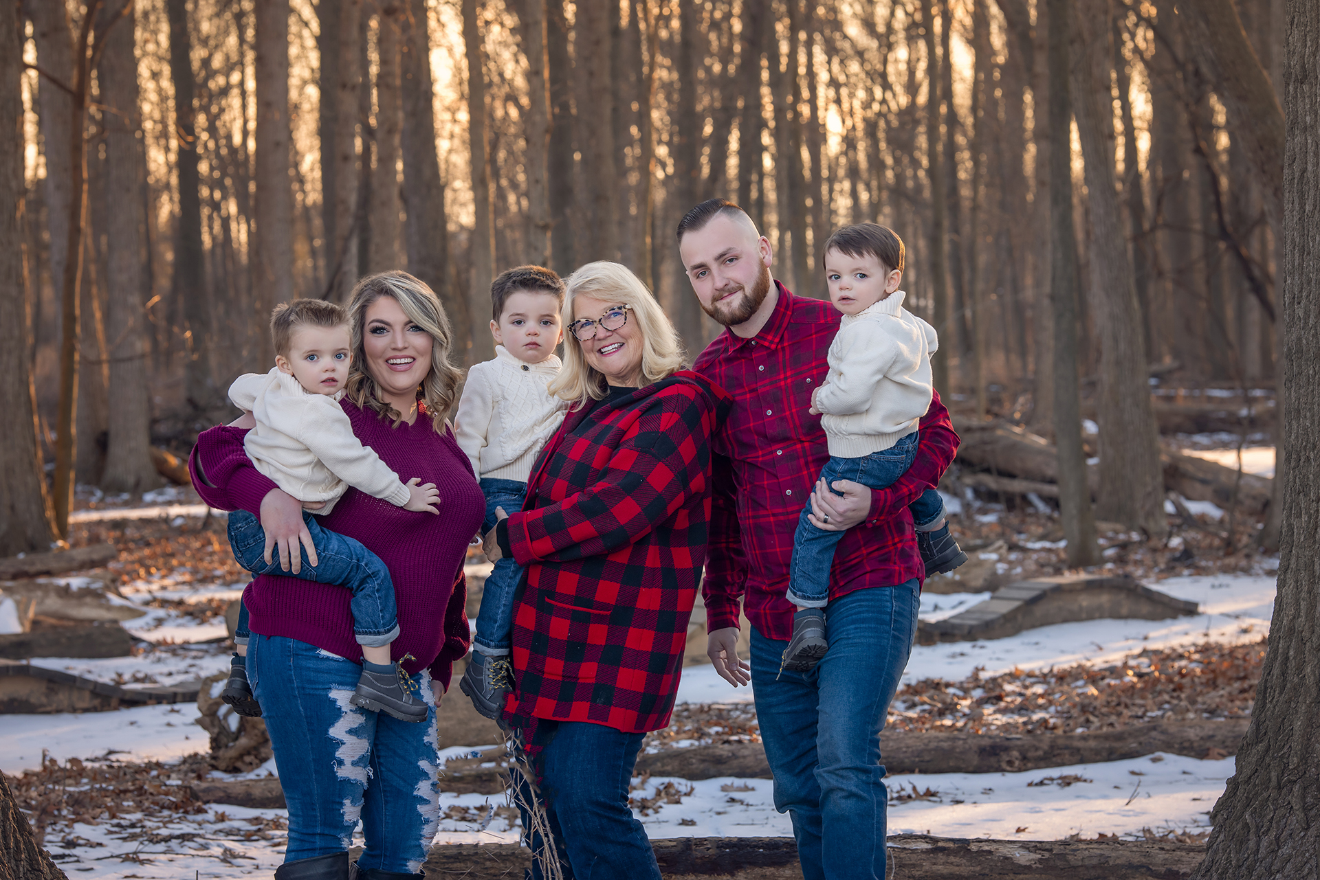 Three adults and three children pose among a snowy woodland landscape wearing coordinating red and white outfits for a family holiday photoshoot in Detroit.