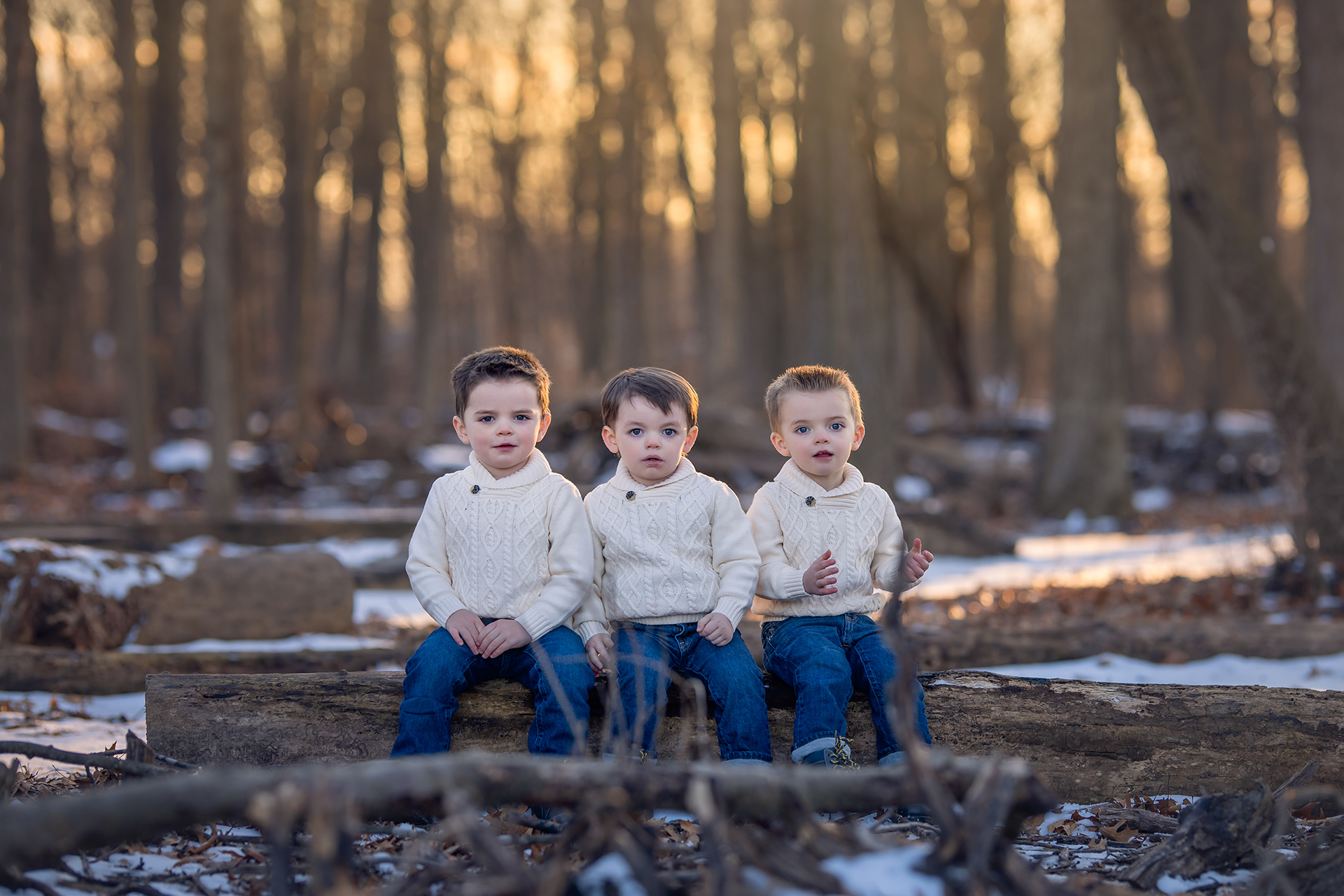 Three children pose among a snowy woodland landscape wearing coordinating white outfits for a family holiday photoshoot in Detroit.