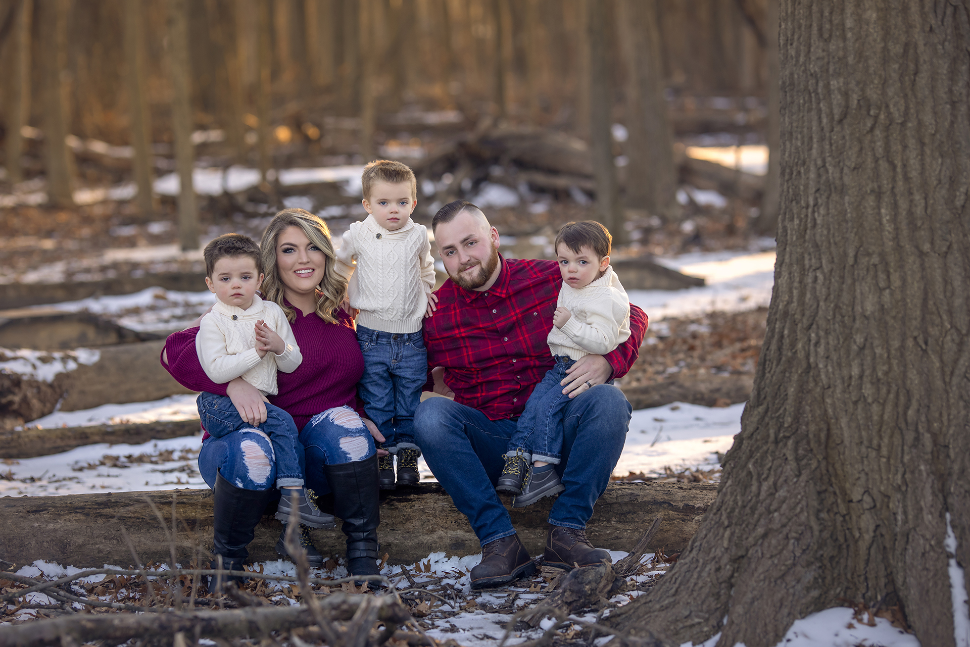 A couple and their three children pose among a snowy woodland landscape wearing coordinating red and white outfits for a family holiday photoshoot in Detroit.