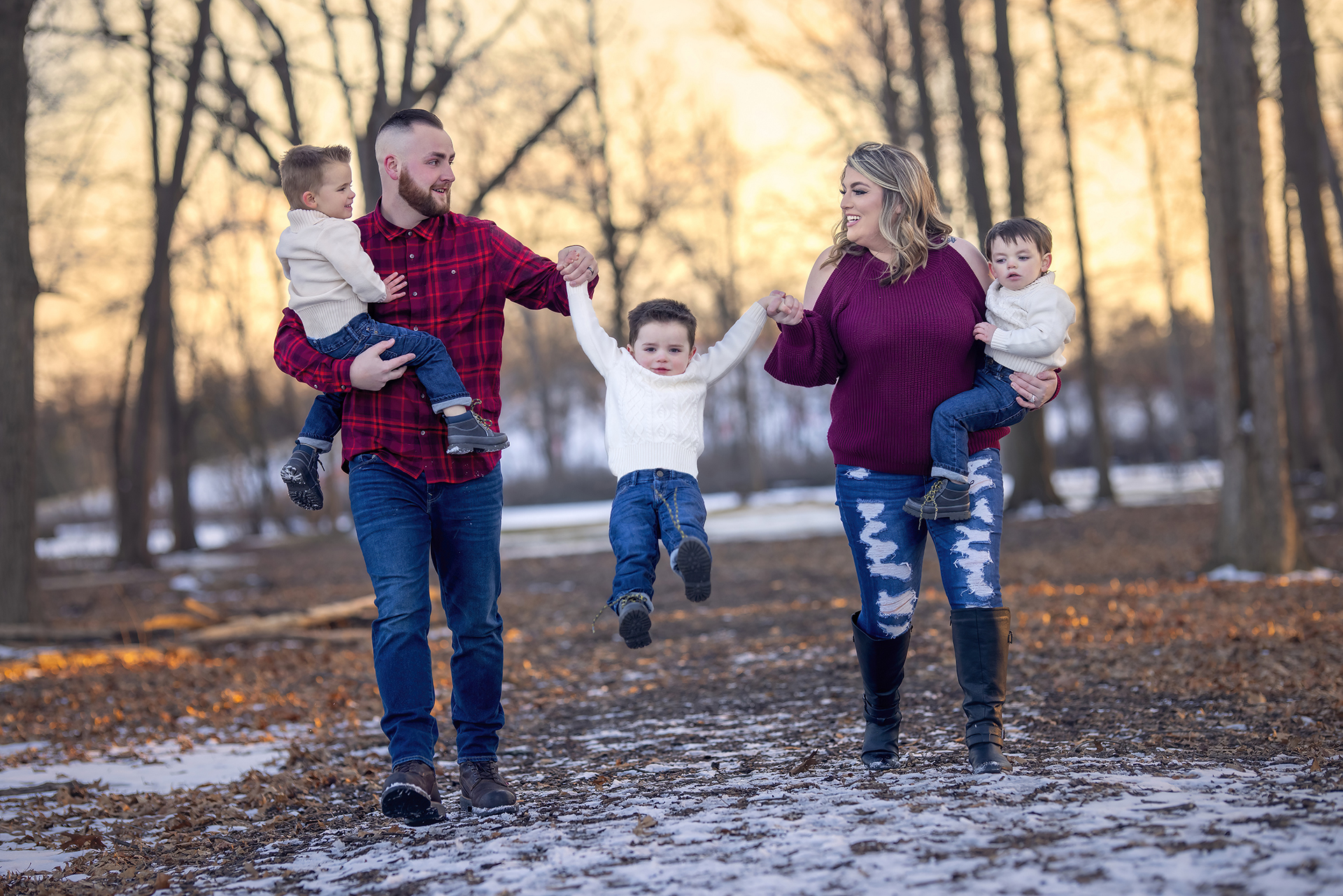 A holiday portrait of a couple holding hands with their young child and lift them in the air while walking along a park trail in Detroit.
