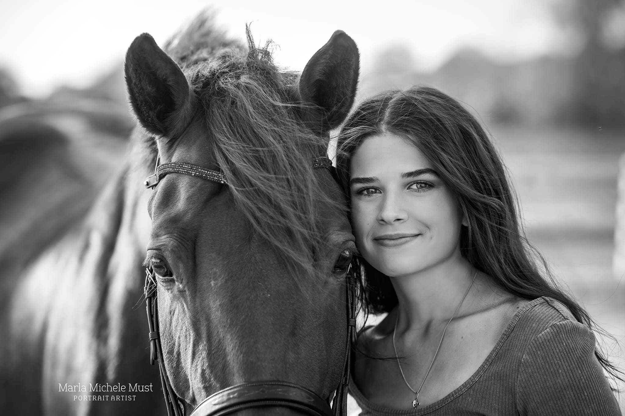 Black and white horse owner portrait for a Detroit equine photographer: Leaning close to her horse's face with care and smiles happily at the camera.