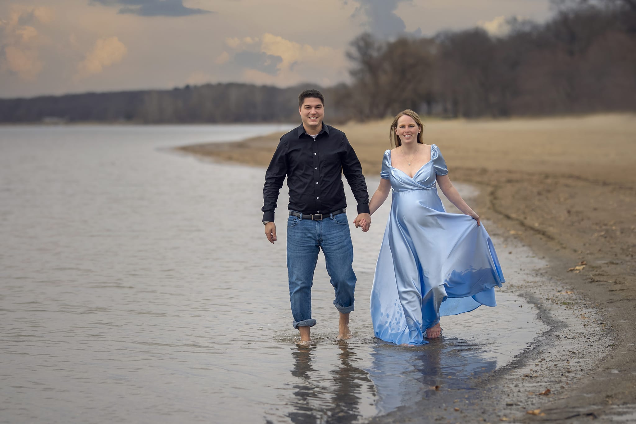 A pregnant woman and her partner walk along a Michigan beach for a maternity photoshoot; a moment captured by a skilled maternity photographer.