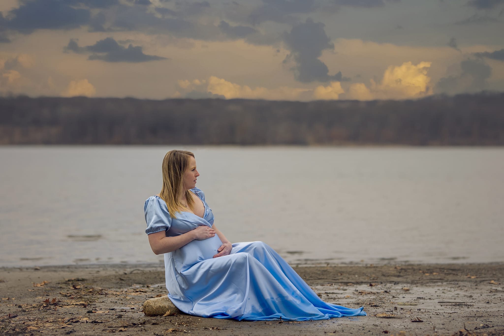 A pregnant woman sits on a Michigan beach for a maternity photoshoot; a moment captured by a skilled maternity photographer.