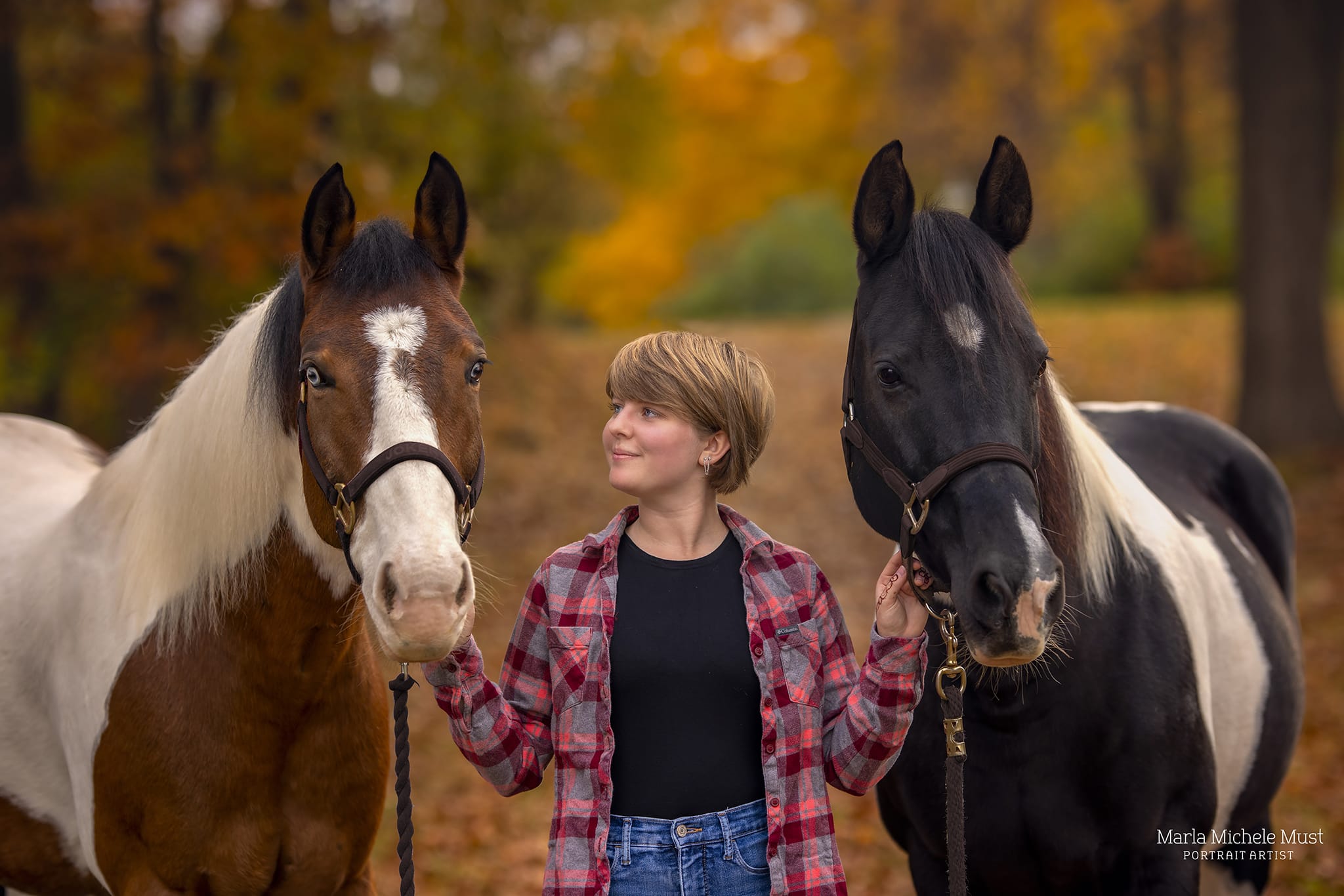 Detroit equine photographer's portrait: Horse owner confidently leading two horses on a trail, holding their reins, looking up at them lovingly.