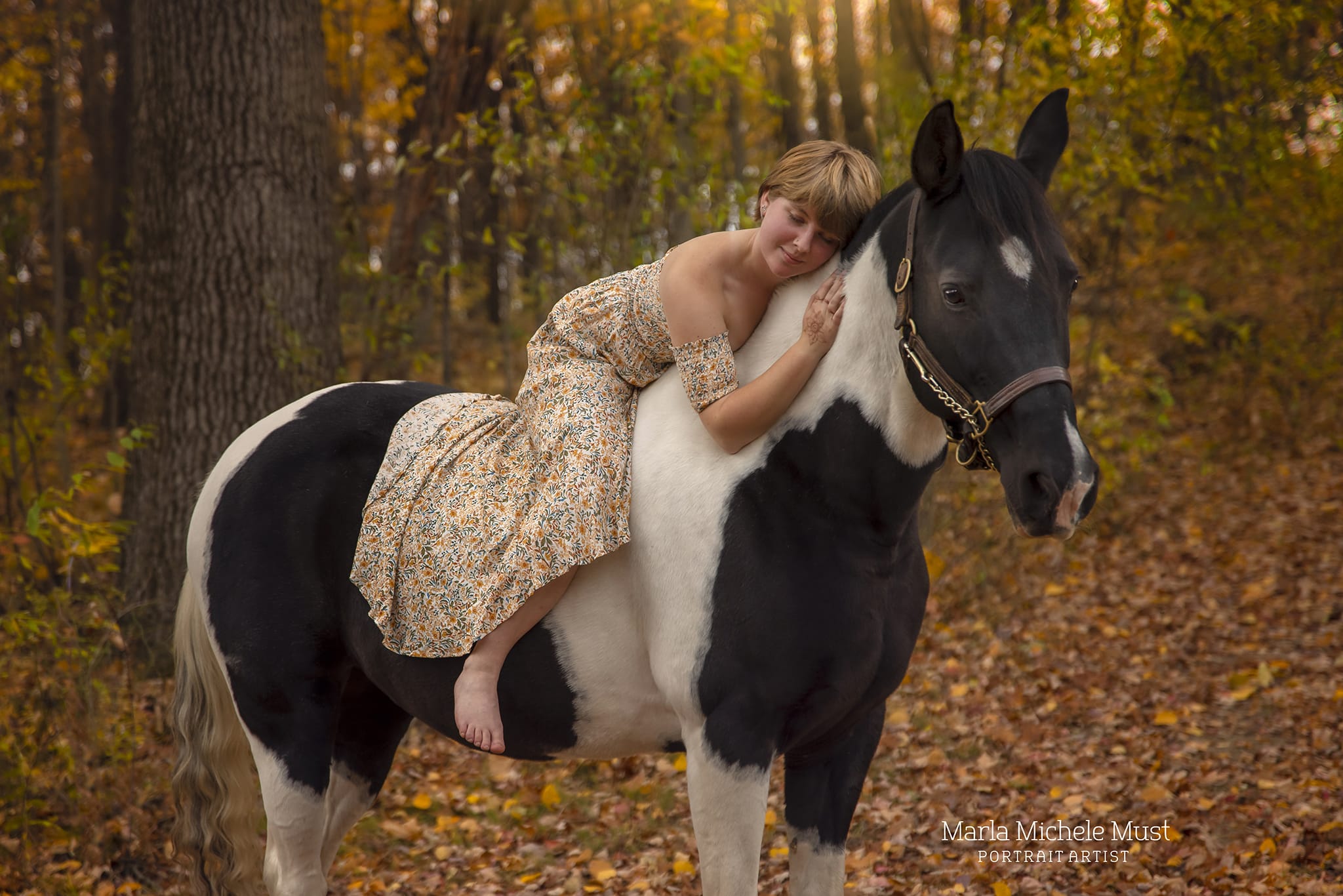 A tender moment in autumn captured by a Detroit equine photographer, conveying a woman lounging on her horse's back amidst a forest and bed of orange leaves.