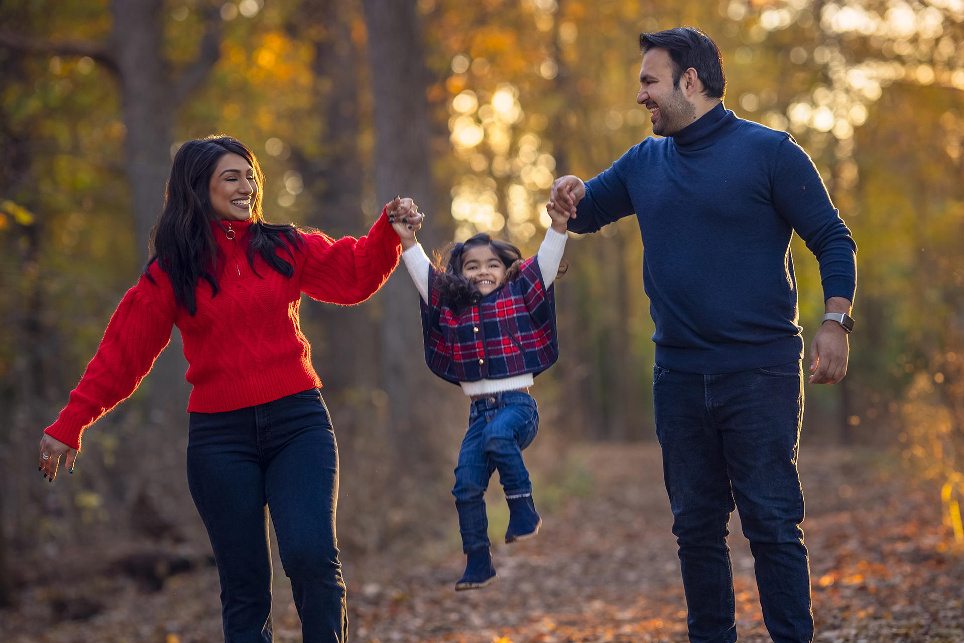 Local Detroit family photographer captures family portrait of a couple walking through the forest with their child, holding hands.