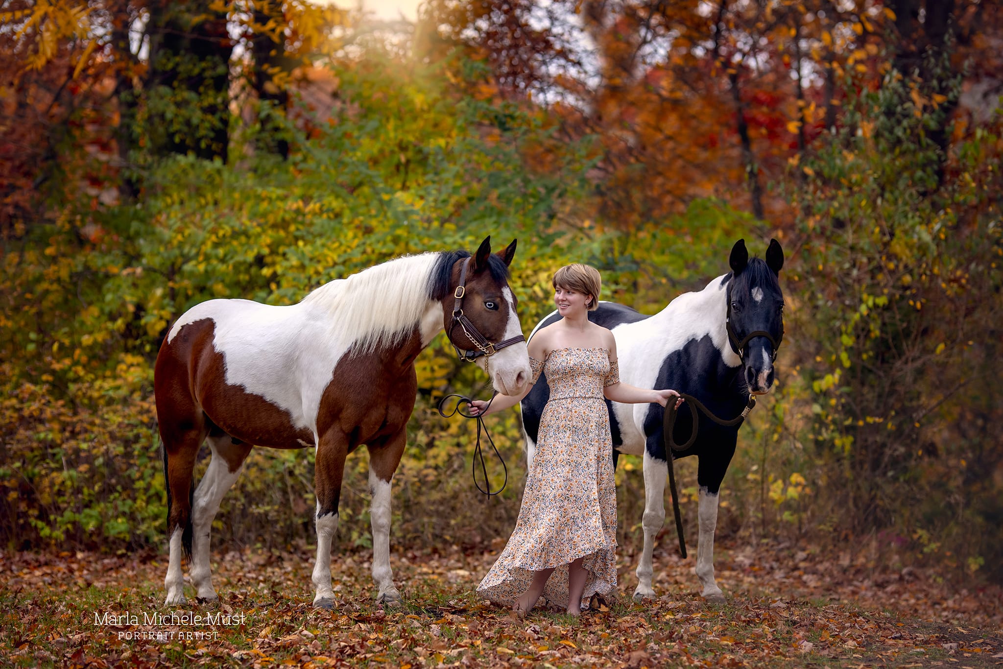 Detroit horse photographer's portrait: Horse rider confidently leading two horses on a trail, holding their reins, looking up at them lovingly.