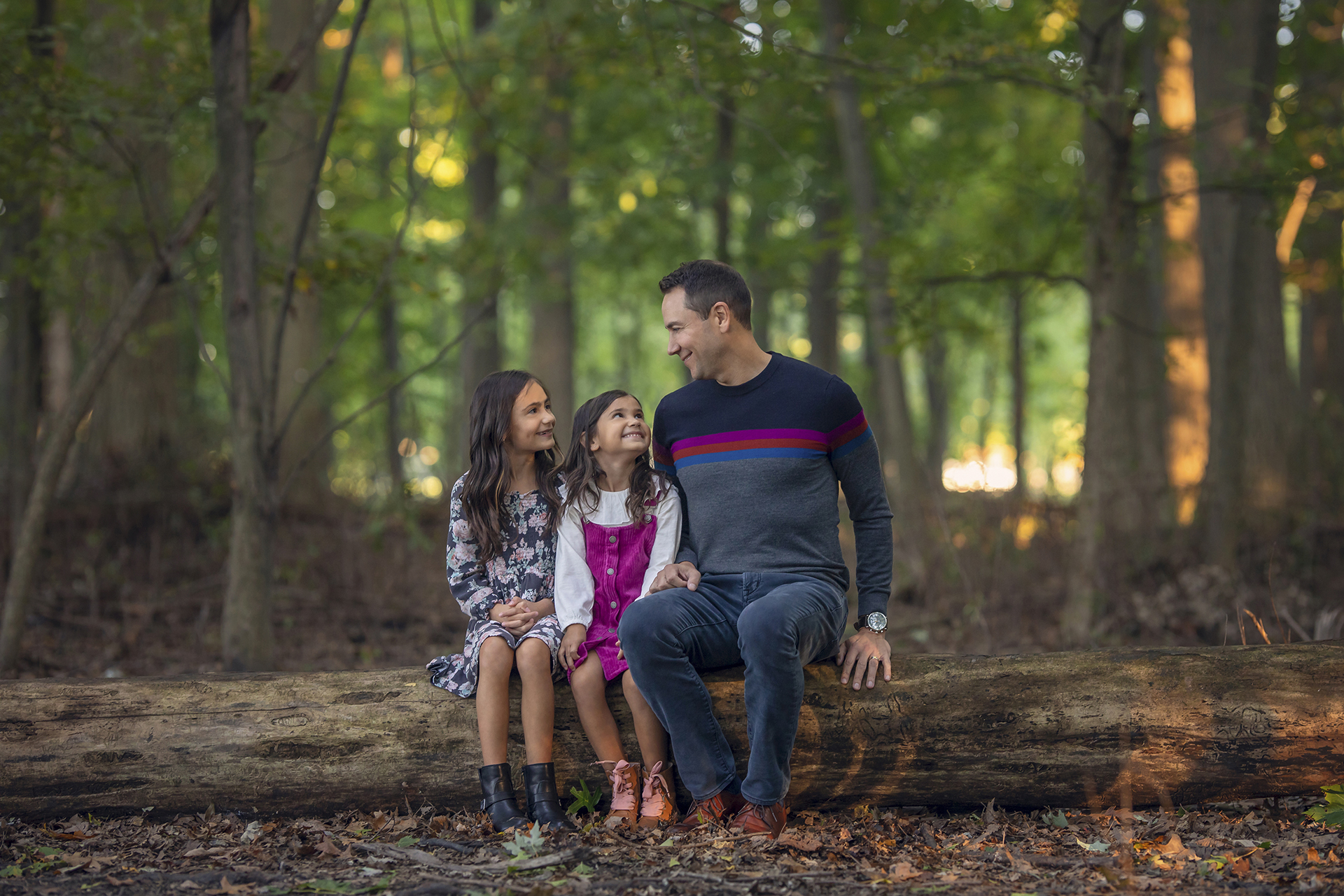 A father sits on a log beside his two daughters for a local family photoshoot in Detroit.