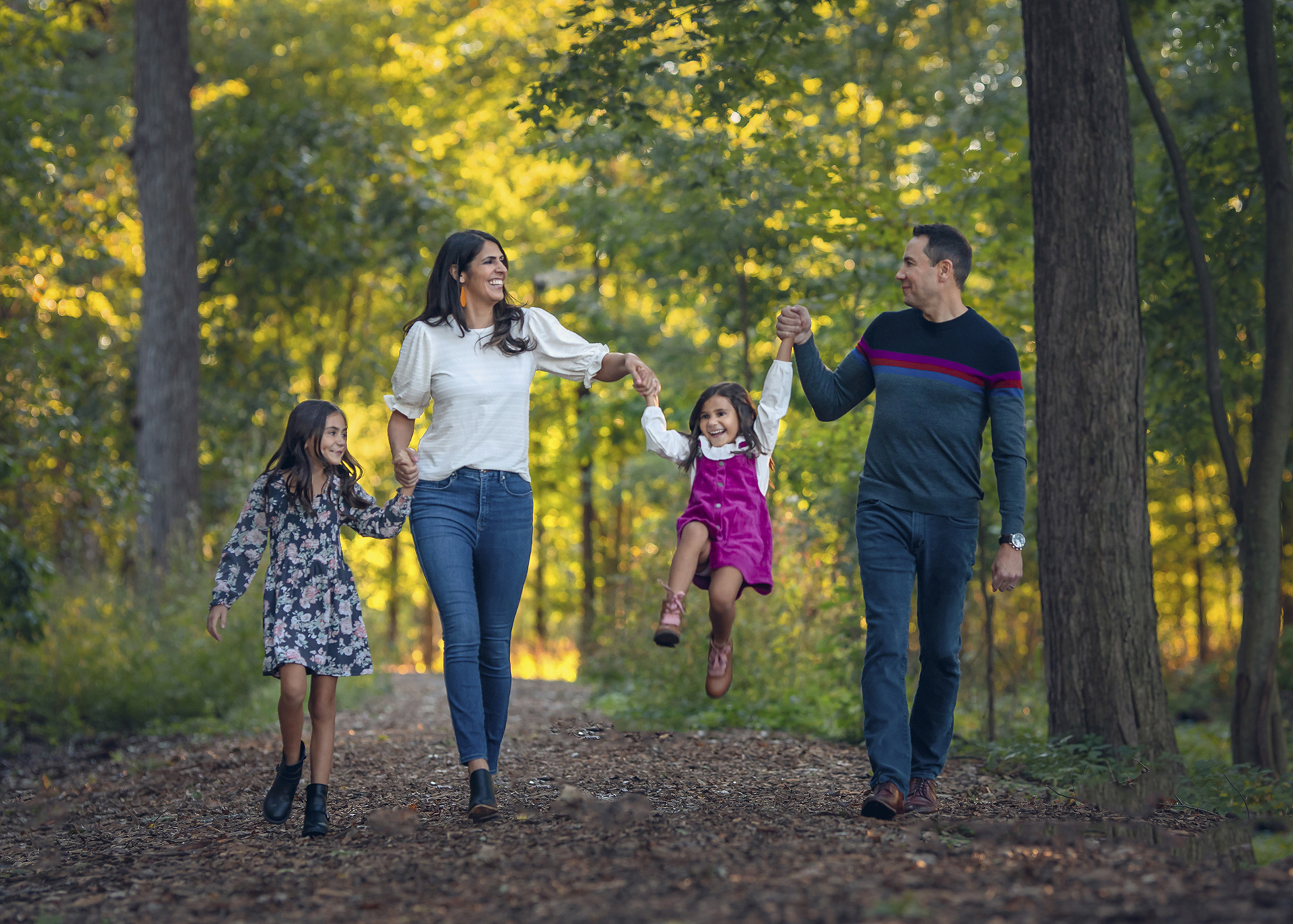 Local Detroit family photographer captures family portrait of a couple walking through the forest with their children, holding hands.