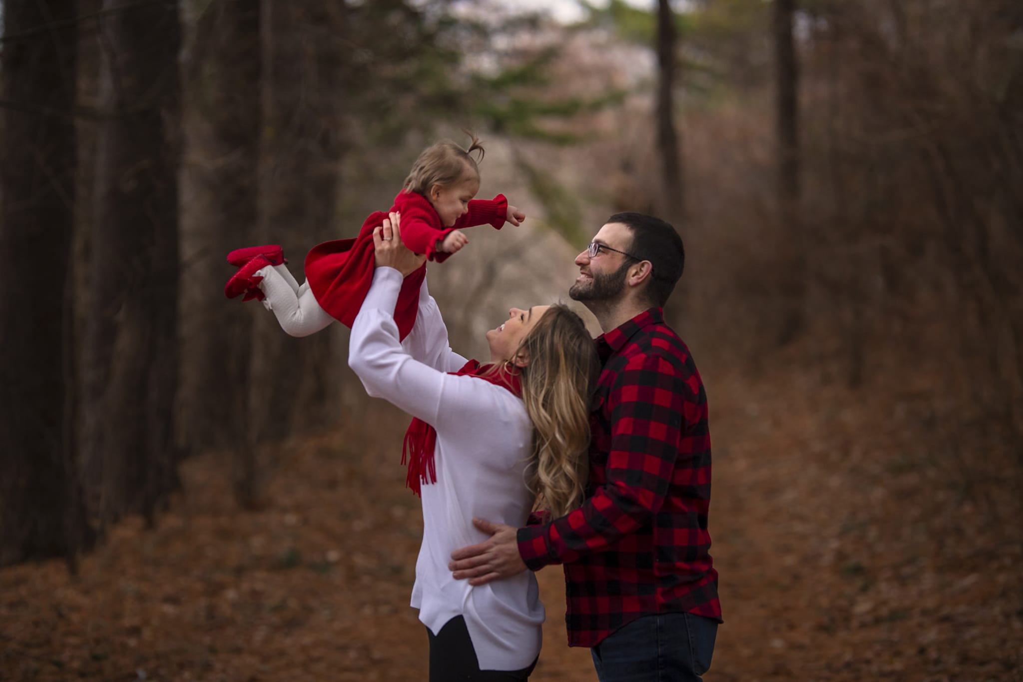 professional family photo in Michigan forest with parents holding baby in action shot