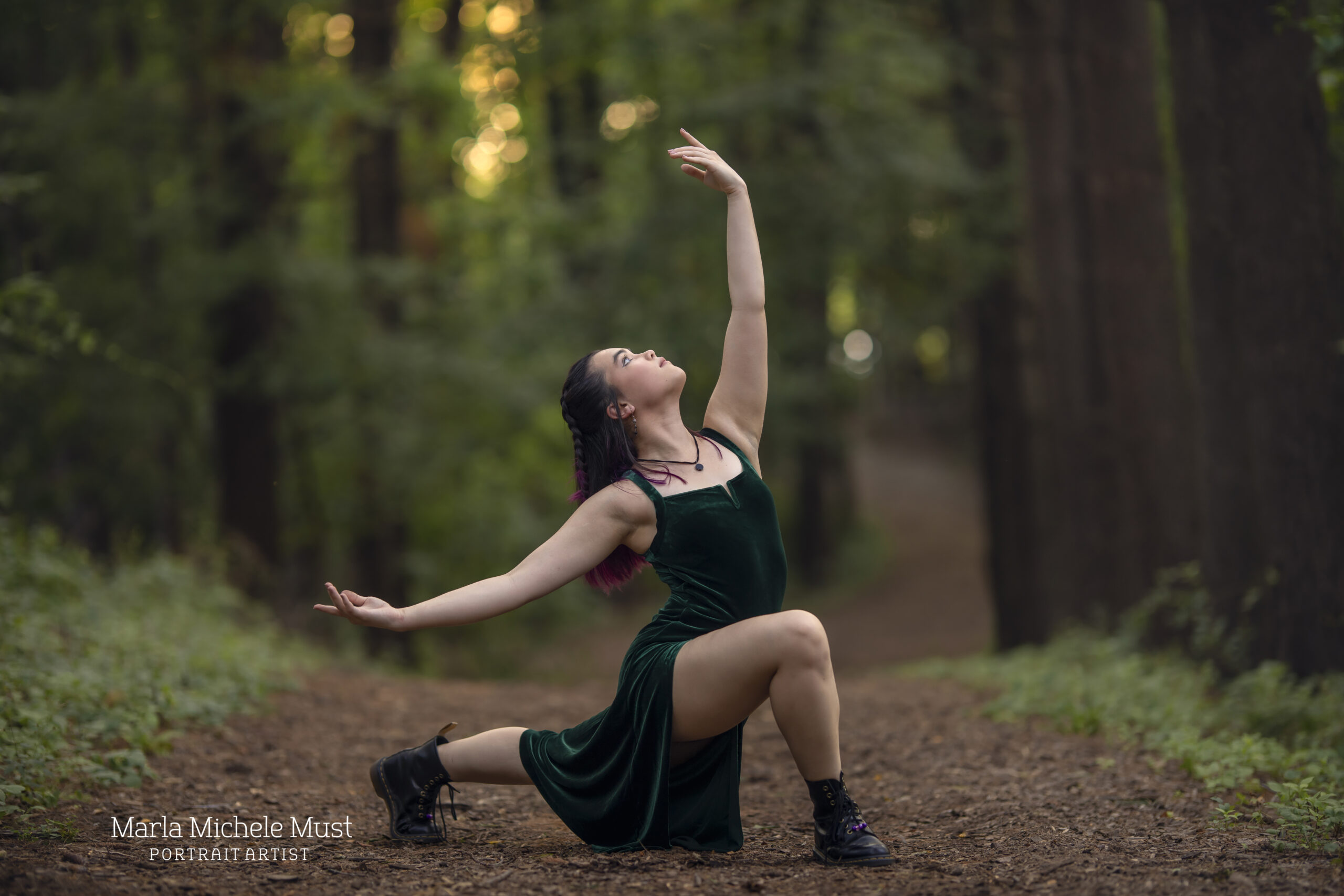 Woman kneels on the ground in a skirt and boots and reaches one arm in the air behind her during a dance photoshoot, taken by a Michigan dance photographer.