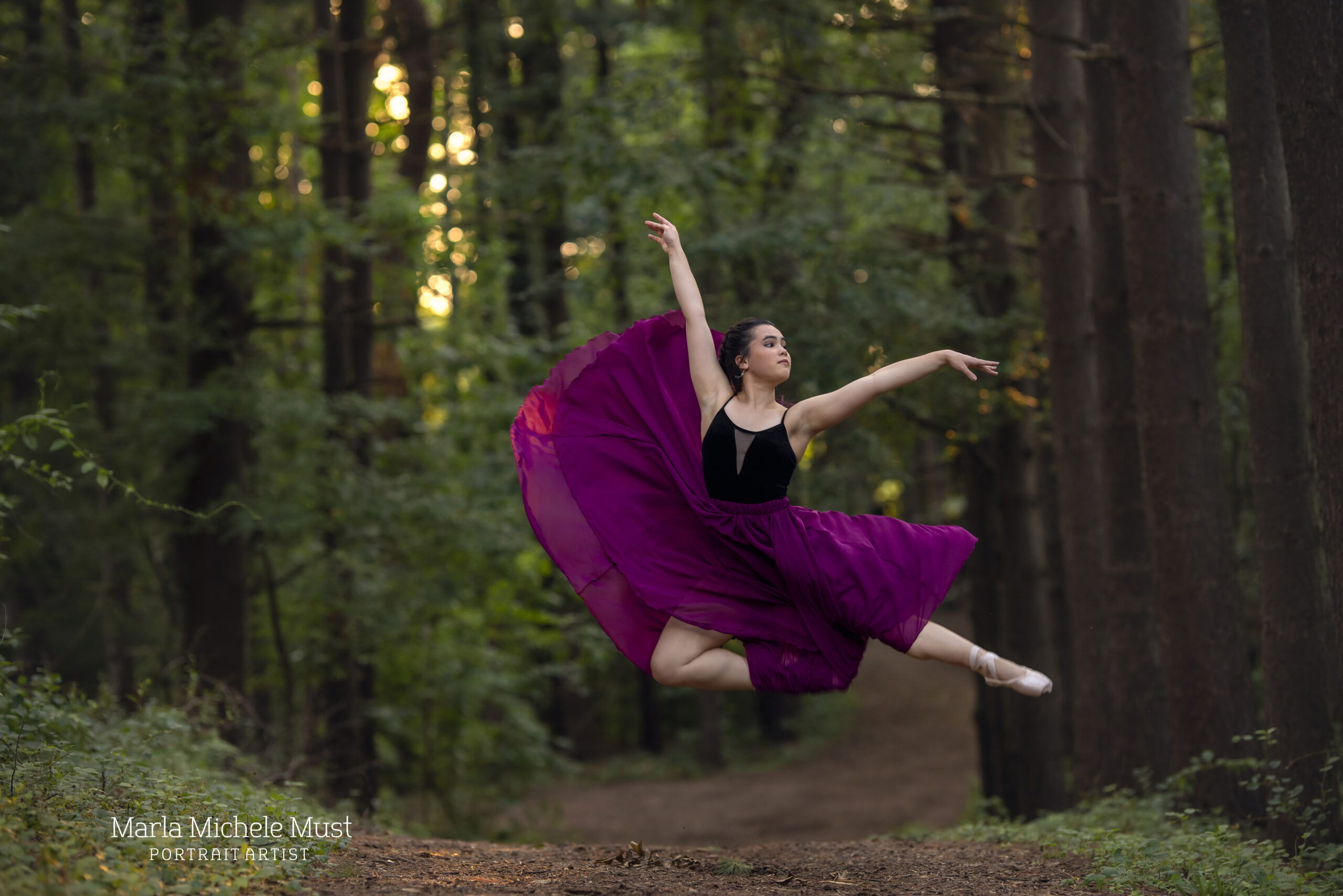 Dancer in a billowy dress jumps in the air on a Detroit forest path during a dance photoshoot, taken by a Michigan dance photographer.