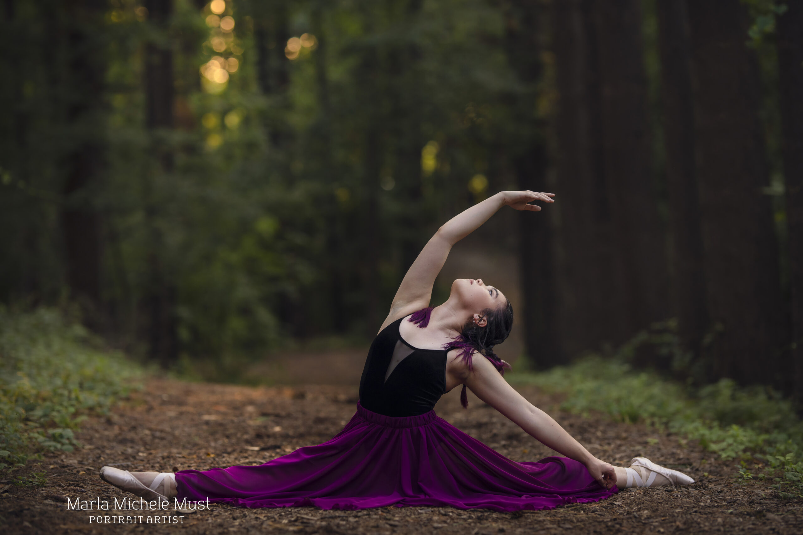 Woman in a flowy skirt does the splits and reaches her arm backwards in the air on a Detroit forest path during a dance photoshoot, taken by a Michigan dance photographer.